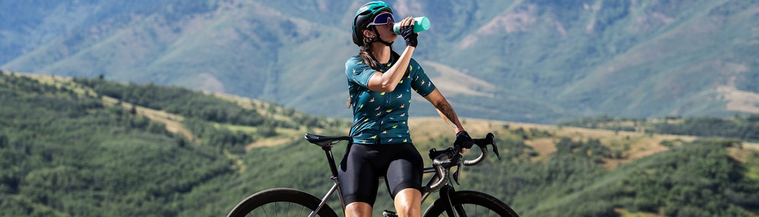 Image d'une femme qui bois dans une gourde en étant sur un vélo.